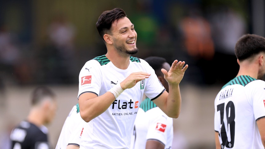 Ramy Bensebaini läuft lachend über den Fußballplatz und hält die Hände zum Abschlagen bereit.