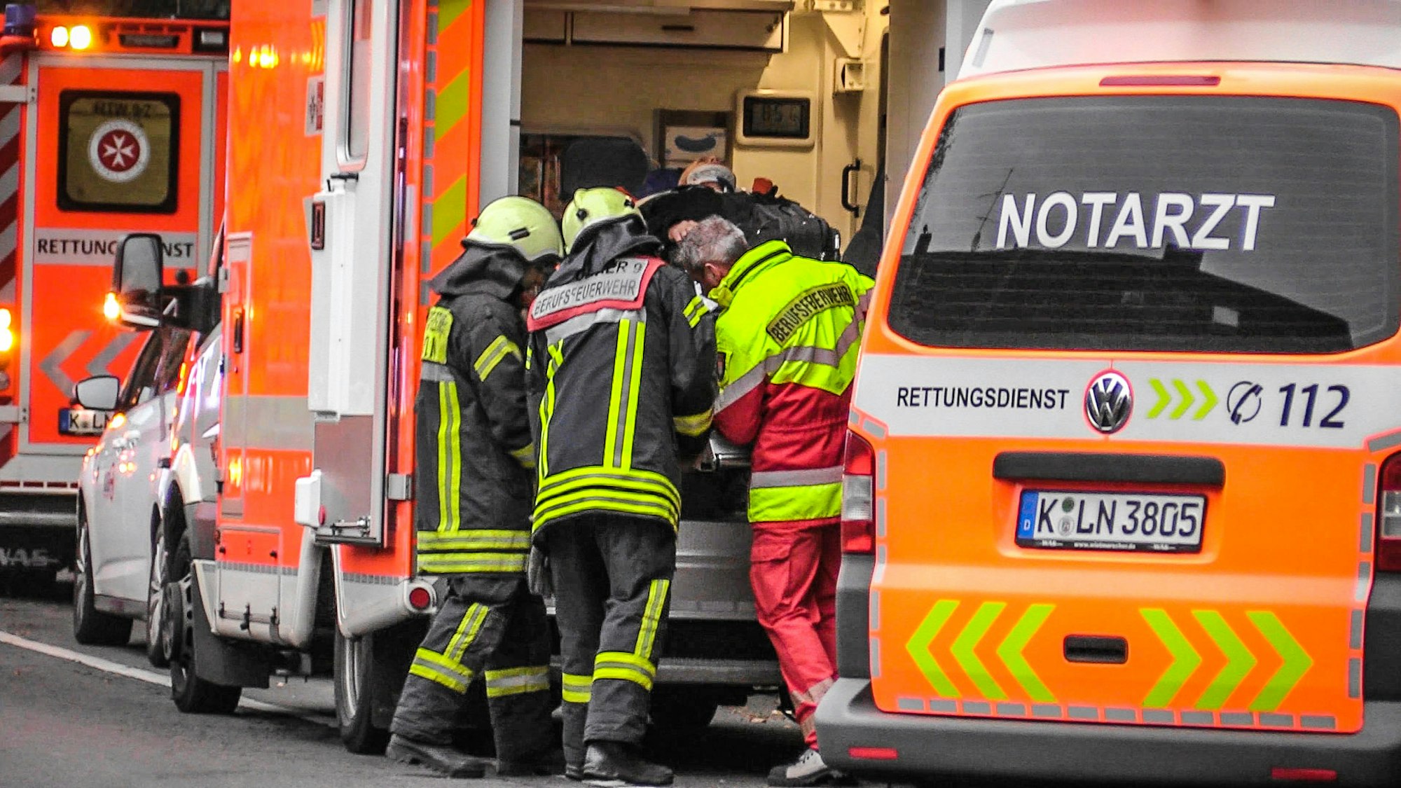 Zwei Feuerwehrmänner und ein Rettungssanitäter schieben eine verletzte Person in den Rettungswagen.