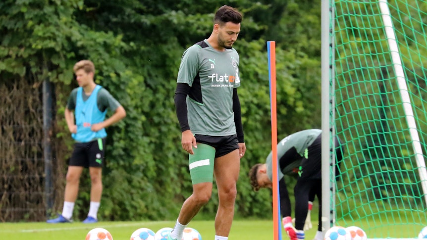 Ramy Bensebaini läuft mit hängendem Kopf und grüner Bandage um den verletzten Oberschenkel vom Trainingsplatz.