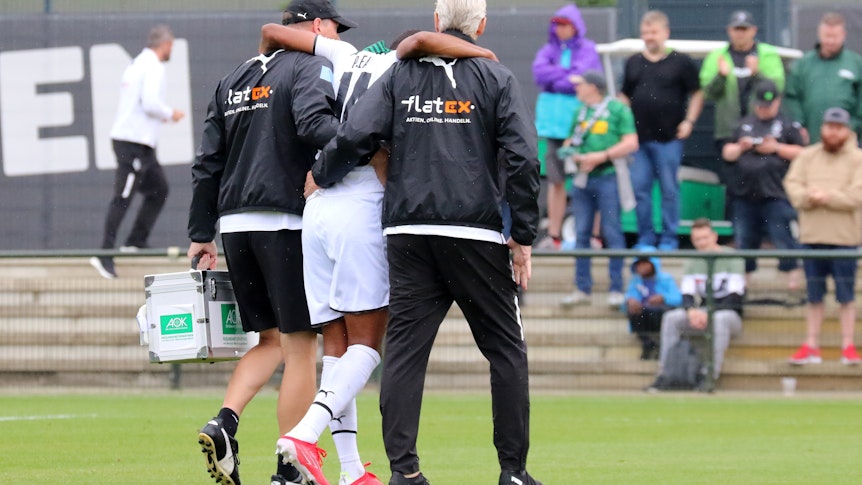 Gladbach-Stürmer Alassane Plea verletzte sich am Samstag (25. Juli 2021) beim Testspiel gegen den FC Metz am Knie und musste das Feld verlassen. Das Foto zeigt ihn humpelnd und gestützt von zwei Borussia-Verantwortlichen.