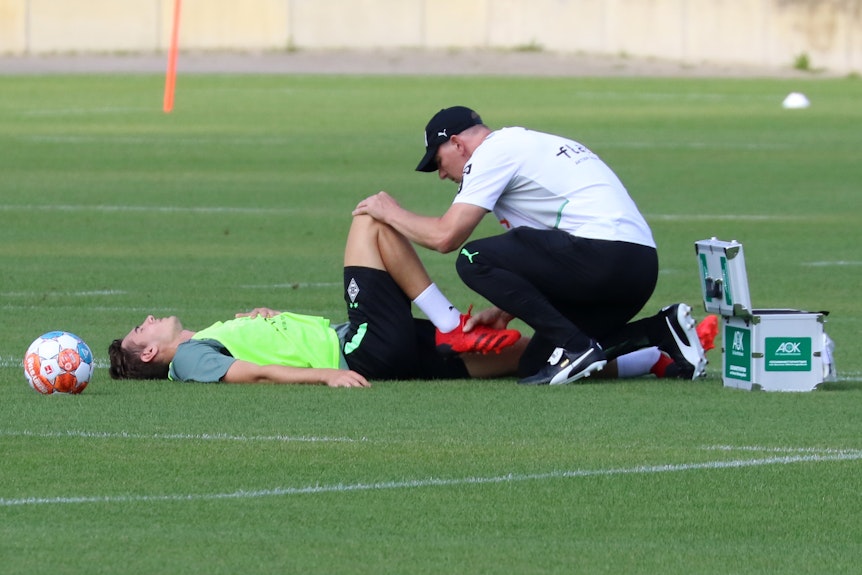 Gladbachs Mittelfeldspieler Florian Neuhaus (auf dem Rasen liegend) muss am Mittwoch (4. August 2021) während der Trainingseinheit von Physiotherapeut Dirk Müller behandelt werden.