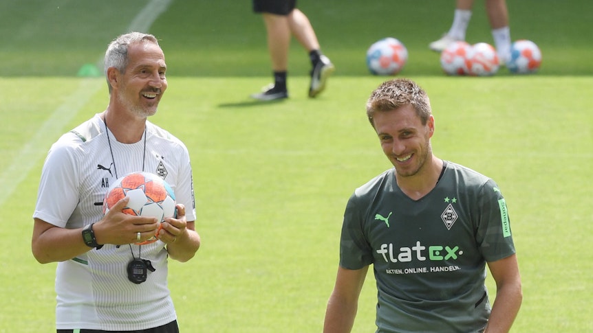 Adi Hütter (l.) mit einem Ball in der Hand und Patrick Herrmann (r.) lachen.