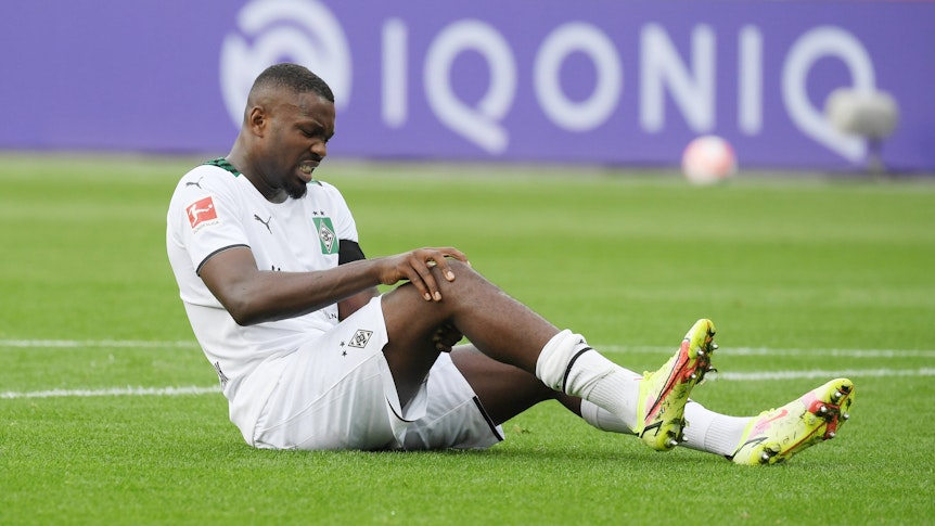 Gladbachs Marcus Thuram sitzt beim Bundesliga-Spiel in Leverkusen am 21. August 2021 verletzt auf dem Feld und hält sich das Knie.