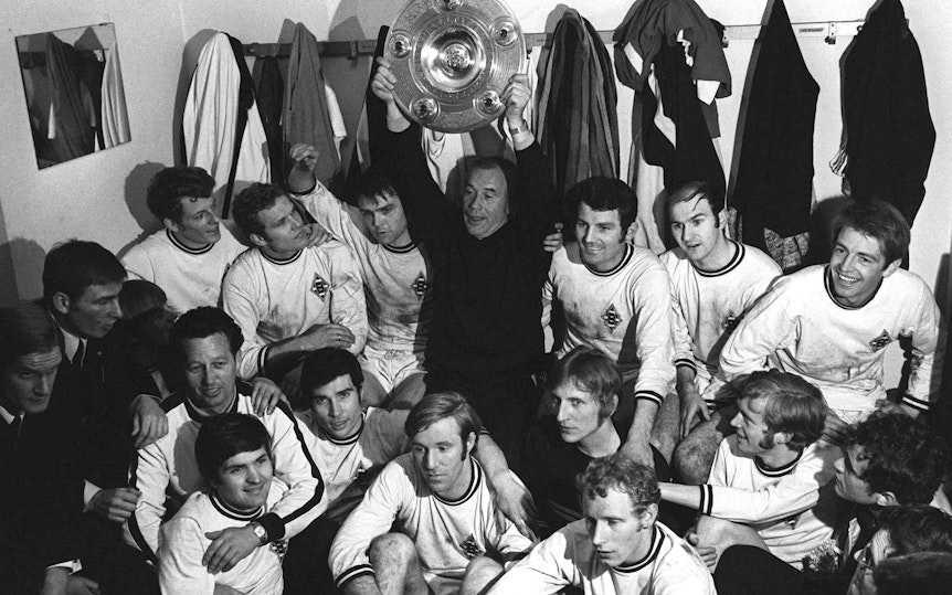 Trainer-Legende Hennes Weisweiler hält, umgeben von seiner Mannschaft, stolz die erste Gladbacher Meisterschale in die Höhe.