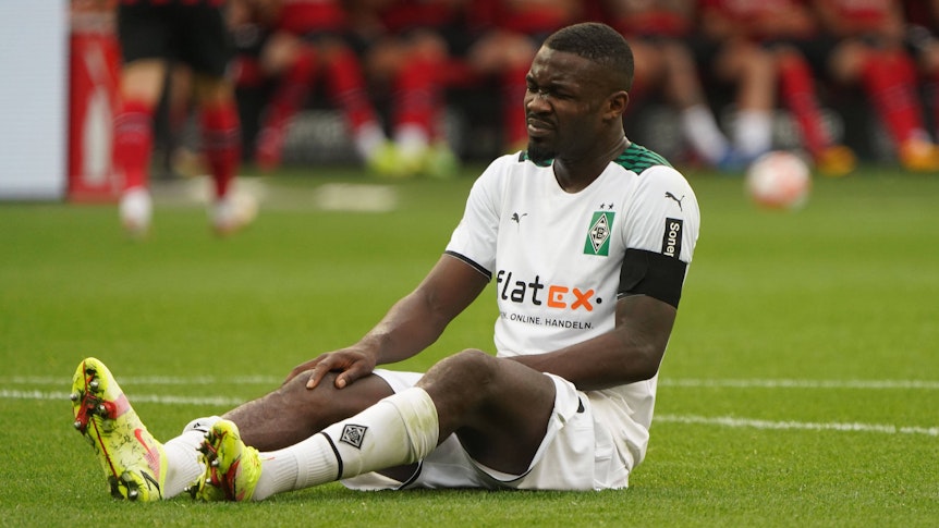 Marcus Thuram von Borussia Mönchengladbach sitzt im Spiel gegen Leverkusen am 21. August 2021 auf dem Boden und hält sich sein verletztes Knie.