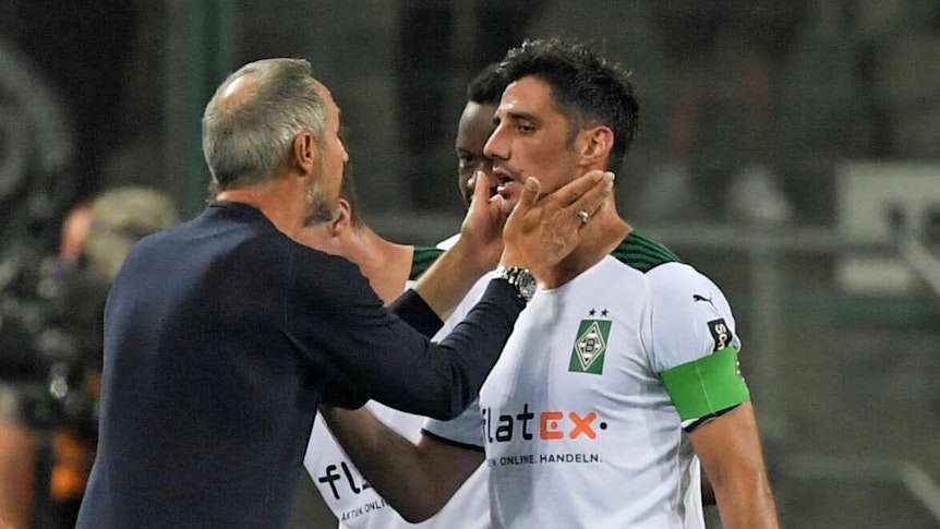 Gladbach-Coach Adi Hütter (l.), jüngst von den Profifußballern in Deutschland zum Trainer der vergangenen Saison gewählt worden, spricht am 12. September 2021 mit seinem Kapitän Lars Stindl, der Borussias Jahrtausend-Torschütze ist. Hütter fasst Stindl mit den Händen ins Gesicht.