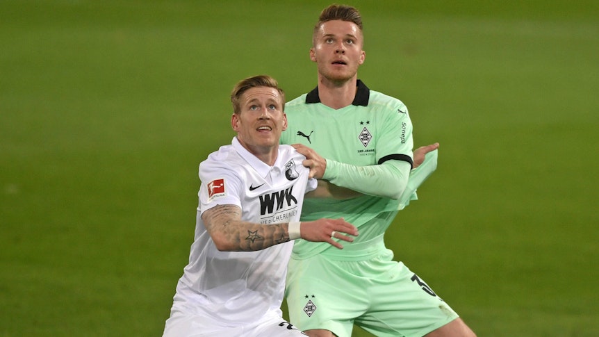 Nico Elvedi (r.), Spieler von Borussia Mönchengladbach und Andre Hahn (l.) blicken im Zweikampf um den Ball nach oben, im Aufeinandertreffen beider Klubs am 12. März 2021.