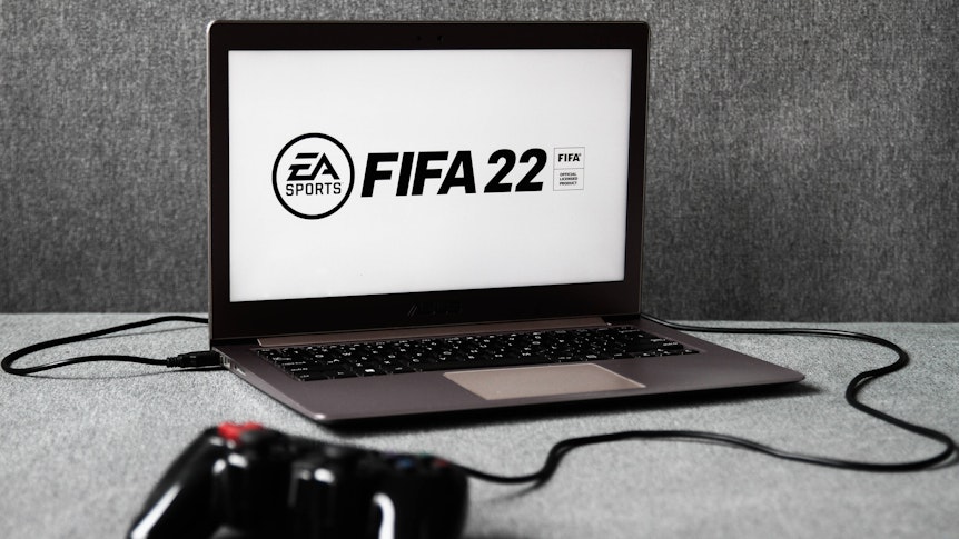 Das Logo des am 1. Oktober 2021 erscheinenden Fußball-Konsolen-Spiels FIFA 22 ist auf einem Laptop zu sehen, an den ein Controller angeschlossen ist.