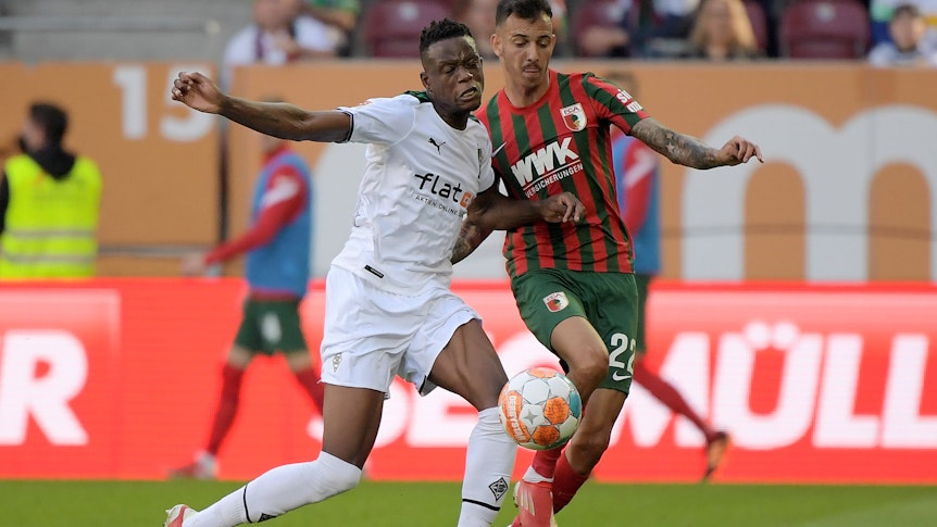 Gladbach-Profi Denis Zakaria (l.) im Duell mit Amaral Borduchi Iago (r.) vom FC Augsburg beim Bundesliga-Duell am 18. September 2021 in der Augsburger Arena. Beide kämpfen um den Ball.