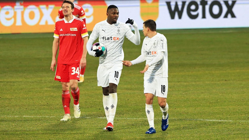 Die Gladbacher Profis Marcus Thuram (M.) und Stefan Lainer (r.) unterhalten sich beim Bundesliga-Remis in Berlin am 30. Januar 2021 auf dem Spielfeld, Thuram trägt dabei den Ball in seinen Händen.