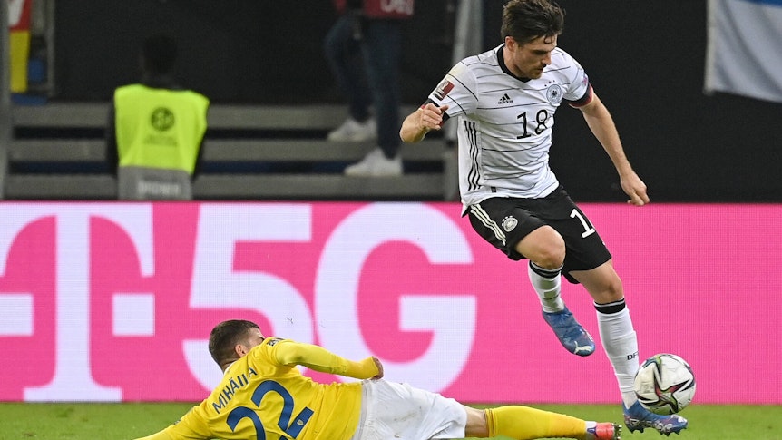 DFB-Nationalspieler Jonas Hofmann (r.), bei Fußball-Bundesligist Borussia Mönchengladbach unter Vertrag, behauptet im Duell mit Valentin Mihaila (l.) den Ball während des Länderspiels gegen Rumänien am 8. Oktober 2021 in Hamburg. Hofmann springt über das Bein des Gegenspielers.
