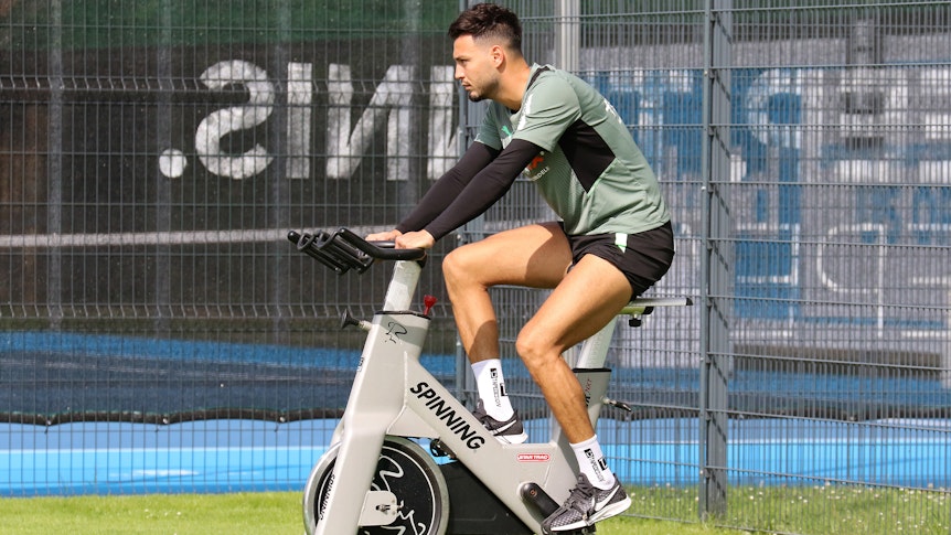 Ramy Bensebaini von Borussia Mönchengladbach sitzt am 18. Juli 2021 auf einem Spinning-Rad während des Trainingslagers in Harsewinkel. Bensebaini schaut nach vorne und radelt.