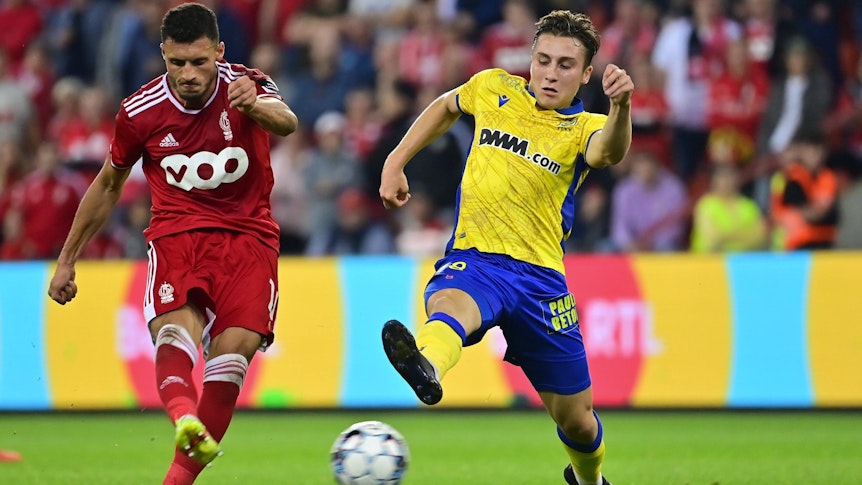 Borussia Mönchengladbach hat Rocco Reitz (r.) an den belgischen Erstligisten VV St. Truiden ausgeliehen. In dieser Szene ist der Mittelfeldspieler am 25. September 2021 in Lüttich im Duell mit Selim Amallah (l.) von Standard Lüttich zu sehen. Reitz streckt sein Bein aus und will einen Schuss blockieren.