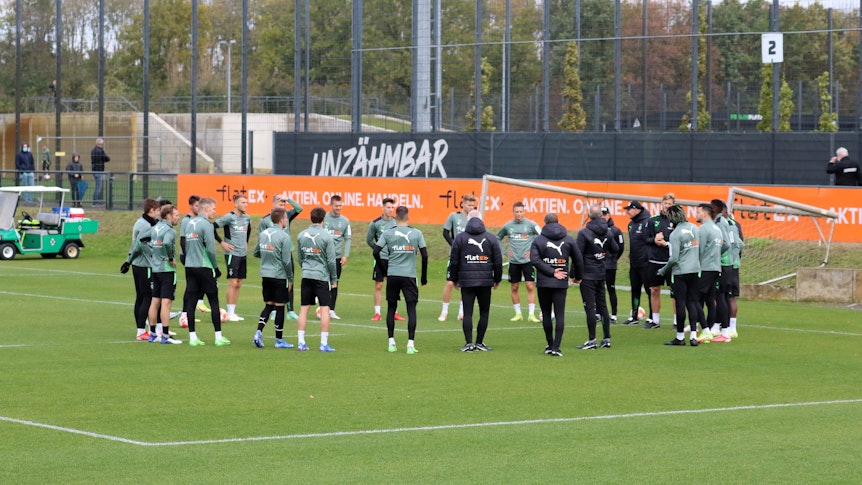 Die Spieler von Borussia Mönchengladbach stehen vor einer Trainingseinheit am 20. Oktober 2021 versammelt auf dem Platz im Borussia-Park, werden dabei von einigen Fans beobachtet.