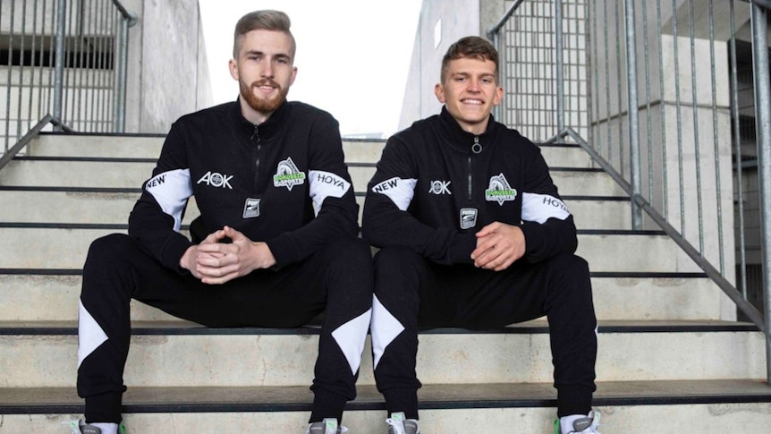 Borussias E-Sportler Yannick Reiners (l.) und Eleftherios „Lefti“ Ilias (r.), sitzen nebeneinander auf den Stufen im Borussia-Park und peilen die Meisterschaft an.