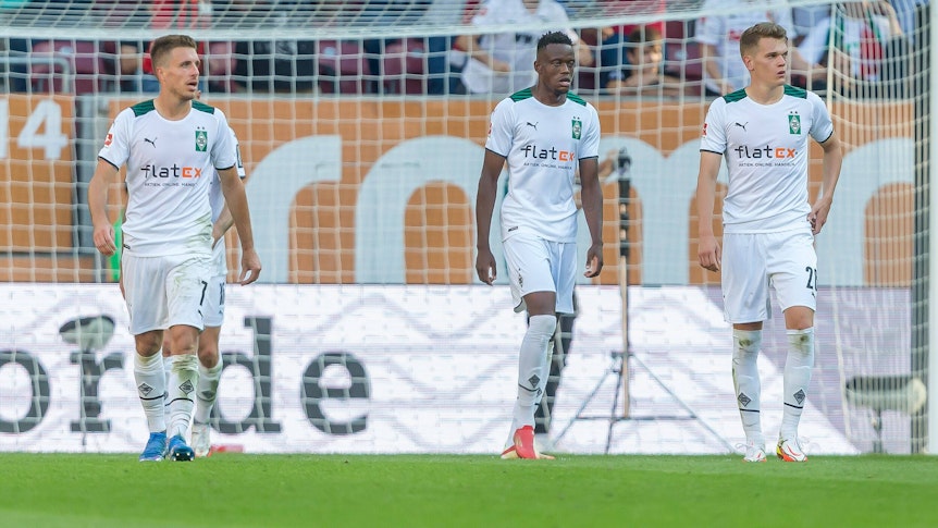 Patrick Herrmann (l.), Denis Zakaria (Mitte) und Matthias Ginter (r.) von Borussia Mönchengladbach verlassen nach der Auswärtsniederlage beim FC Augsburg am 18. September 2021 mit gesenkten Köpfen den Platz der WWK-Arena.