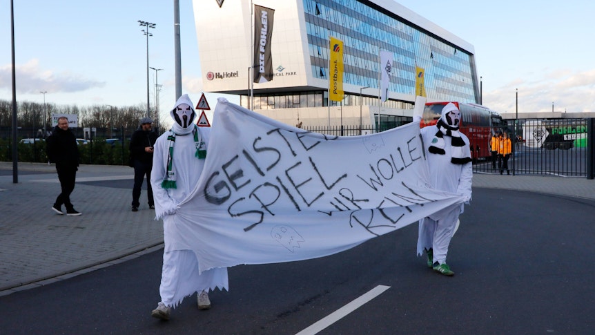 Als Geister verkleidete Gladbach-Fans halten am 11. März 2021 auf dem Gelände im Borussia-Park ein Transparent mit der Aufschrift: "Geisterspiel - Wir wollen rein" hoch.
