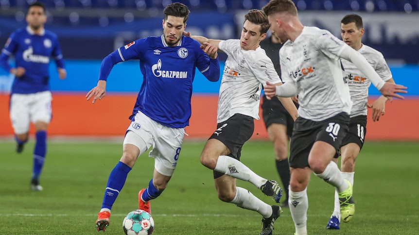 Gladbachs Nationalspieler Florian Neuhaus (Mitte) im Zweikampf mit Schalkes Suat Serdar (l.) beim Bundesliga-Topspiel am 20. März 2021 in Gelsenkirchen.