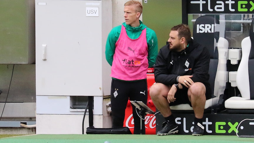 Trauriger Tag für Gladbachs Oscar Wendt (l.), hier beim Bundesliga-Match-Spiel gegen den VfB Stuttgart am Samstag (15. Mai) auf der Bank neben Co-Trainer René Maric (r.). Der Linksverteidiger sah eine 1:2-Niederlage seines Teams und kam trotz Abschied vom Niederrhein nach zehn Jahren nicht mehr zum Einsatz.