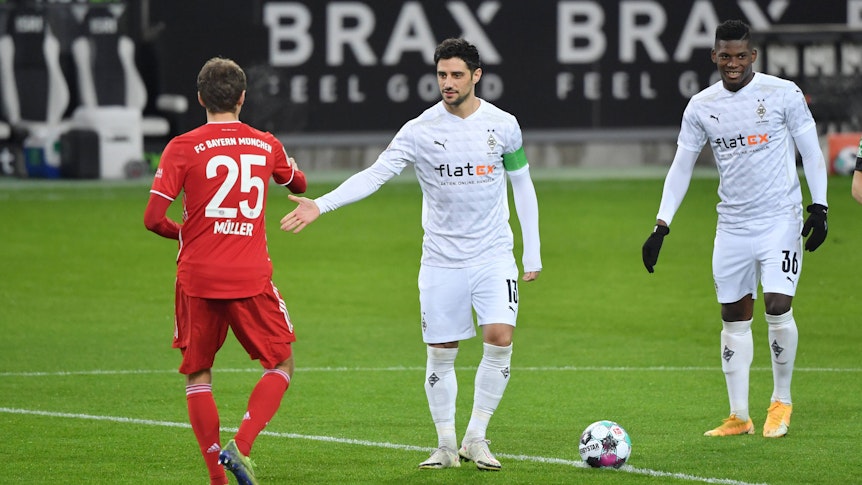Gladbach-Kapitän Lars Stindl klatscht sich am 8. Januar 2021 am Mittelkreis mit Bayern-München-Star Thomas Müller (l.) ab, derweil schaut Fohlen-Stürmer Breel Embolo (r.) zu.