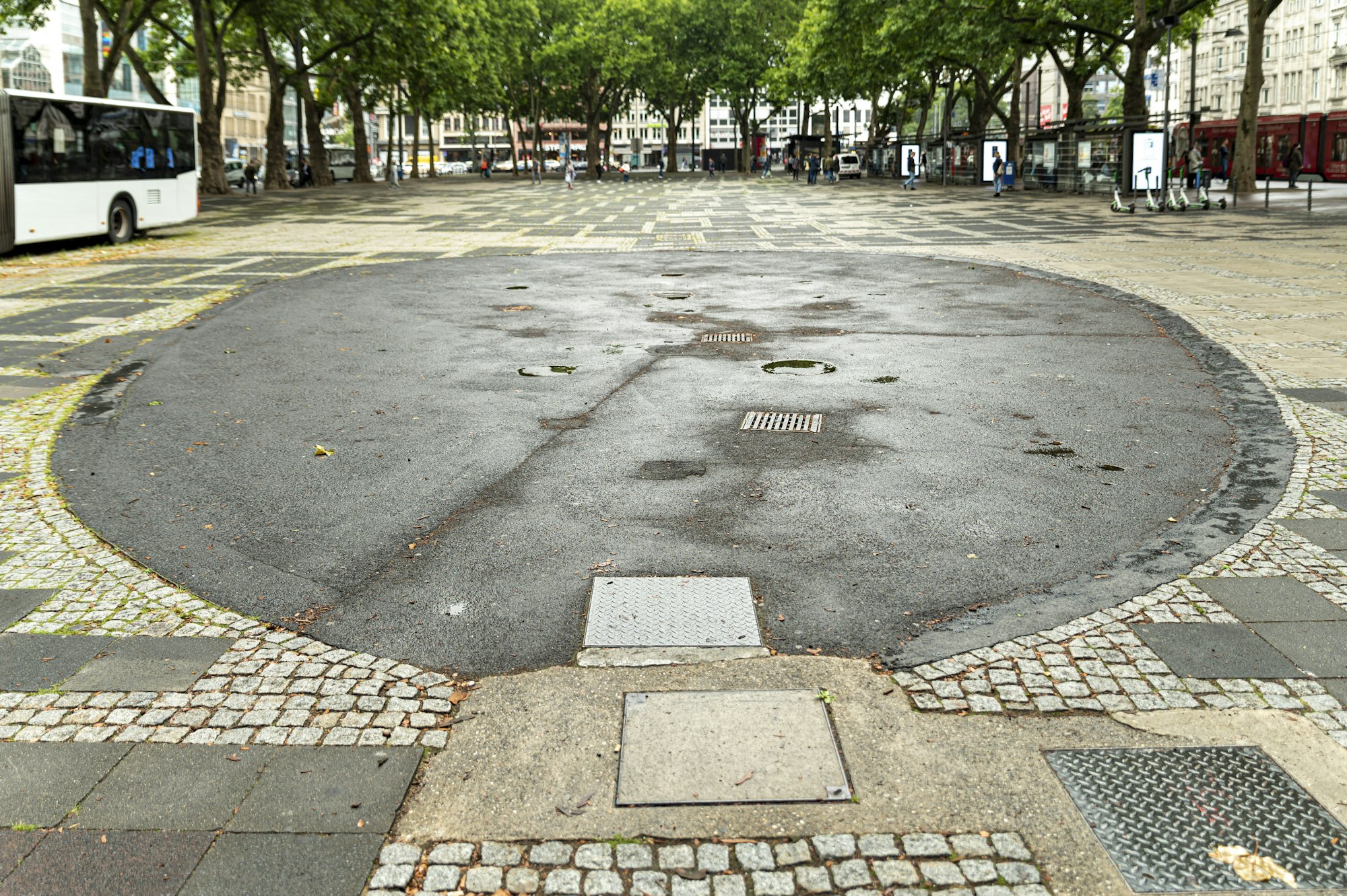 Ein Brunnen auf dem Neumarkt in Köln ist mit Bitumen verfüllt worden, so dass von ihm nur noch eine runde Fläche übrig ist.