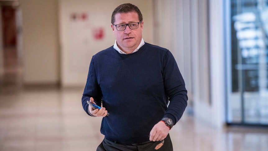 Gladbach-Manager Max Eberl schreitet voran und hält in seiner rechten Hand ein Smartphone.
