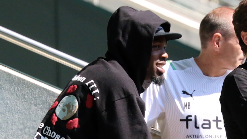 03.07.2021, Mönchengladbach, Marcus Thuram sitzt auf der Tribüne des Borussia-Park-Stadions und lächelt.