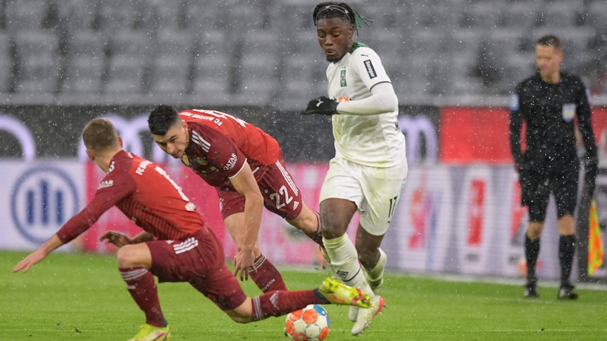 Manu Kone (r.), Mittelfeldakteur von Borussia Mönchengladbach, setzt sich im Bundesliga-Duell bei Bayern München (7. Januar 2022) gegen zwei Gegenspieler durch. Kone dribbelt mit dem Ball.