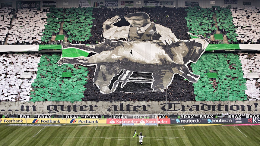 Bei einer Choreografie der Gladbach-Fans im Borussia-Park (14. Februar 2015) versohlt ein Borusse dem Kölner Geißbock den Hintern. Auf dem Spielfeld steht Fohlen-Maskottchen Jünter.