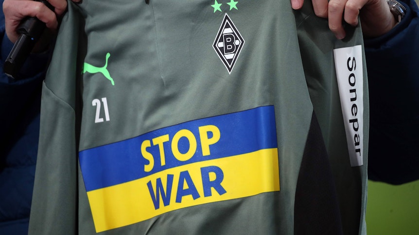 Um dieses schöne Stück geht es. Die Aufwärmshirts von Borussia Mönchengladbach mit der Botschaft „Stop War“ stehen noch zur Auktion. Das Shirt wird in die Kamera präsentiert.