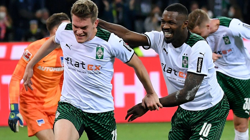 Borussia-Mönchengladbach-Stürmer Marcus Thuram (r.) steht erneut im Fokus einiger europäischer Top-Klubs. Hier bejubelt Thuram zusammen mit Matthias Ginter (l.) den Treffer zum 2:0 gegen Hertha BSC im Borussia-Park (12. März 2022). Marcus Thuram läuft Matthias Ginter lächelnd hinterher und versucht ihn zu greifen.