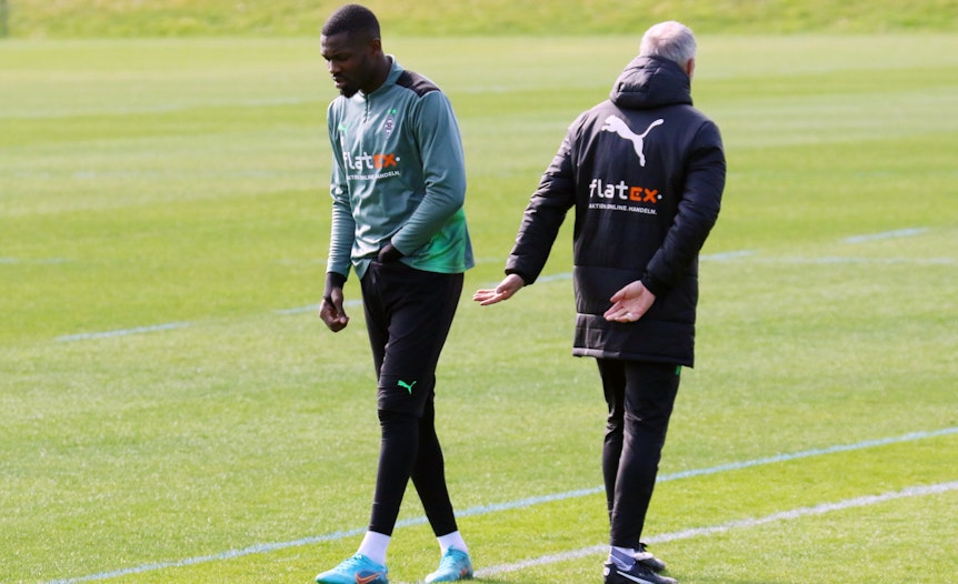 Marcus Thuram (l.) mit Coach Adi Hütter (r.) während einer Trainingseinheit im Borussia-Park am 30. März 2022. Thuram greift sich in die Hose.