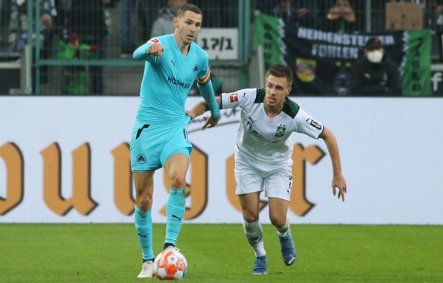 Branimir Hrgota, Ex-Spieler von Borussia Mönchengladbach, im Duell mit Gladbacher-Urgestein Patrick Herrmann in der Partie am 20. November 2021. Hrgota läuft mit dem Ball am Fuß vor Herrmann weg.