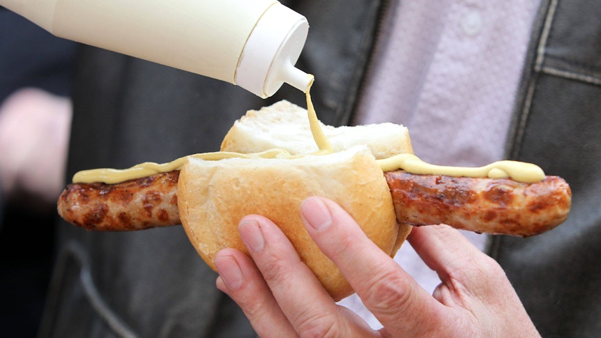 Eine Bratwurst im Brötchen mit Senf. Diese Aufnahme stammt vom 26. März 2021. Auf dem Symbolfoto wird der Senf auf die Wurst aufgetragen.