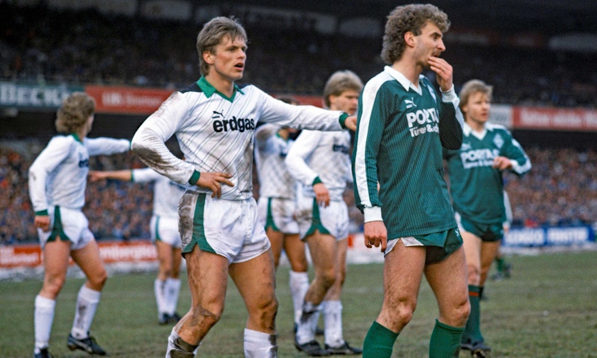 Uli Borowka (l.), ehemaliger Spieler von Borussia Mönchengladbach, hier zu sehen am 21. März 1987 mit Duell mit Werder-Bremen-Stürmer Rudi Völler (r.) im Weserstadion. Völler und Borowka schauen nach vorne in Erwartung einer Hereingabe.