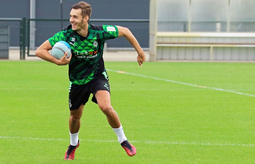 Gladbach-Profi Florian Neuhaus hat sichtlich Spaß beim Rugby. Dieses Foto stammt vom Training am 27. Juni 2022 im Borussia-Park. Neuhaus hält den Rugby-Ball fest und läuft.