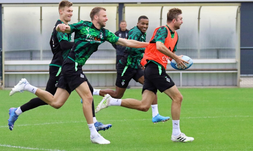 Weltmeister Christoph Kramer (r.) hat sich im Gladbach-Training (27. Juni 2022) das Rugby-Ei geschnappt und wird von Marvin Friedrich, Moritz Nicolas und Alassane Plea verfolgt. Kramer trägt ein orangenes Leibchen.