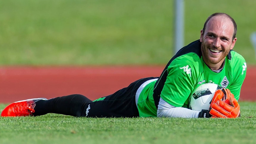 Gladbach-Keeper Tobias Sippel am 18. Juli 2016 im Trainingslager von Borussia Mönchengladbach in Rottach-Egern. Zu diesem Zeitpunkt sah die Frisur noch anders aus. Sippel liegt auf dem Rasen, hält einen Fußball fest und lacht.