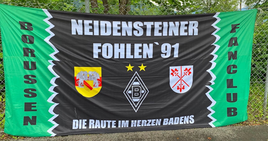 Das Banner des Gladbach-Fanklubs „Neidensteiner Fohlen '91“ ist auf der Sportanlage Birkenmoos in Rottach-Egern zu sehen. Die Fahne hängt an einem Zaun.