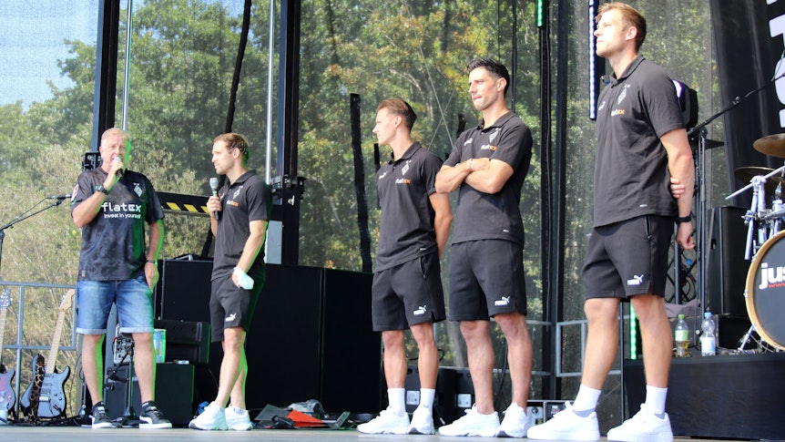 Moderator Frank Schiffers mit den Profis Tony Jantschke, Hannes Wolf, Lars Stindl und Torwarttrainer Fabian Otte (v.l.n.r) am 24. Juli 2022 bei der Saisoneröffnung von Borussia Mönchengladbach. Die Gruppe steht auf einer Bühne, Schiffers und Jantschke sprechen in ein Mikrofon.