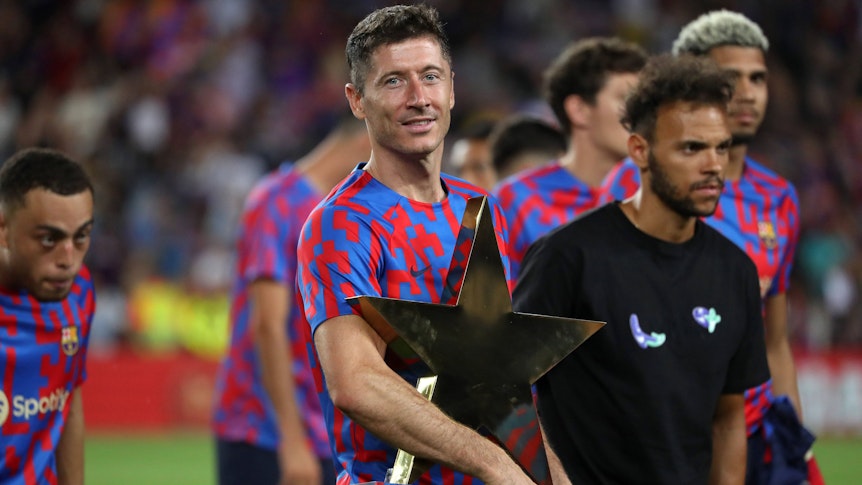 Stürmer Robert Lewandowski, neuer Team-Kollege von Marc-André ter Stegen beim FC Barcelona, hält am 7. August 2022 die Joan-Gamper-Trophäe im Arm. Lewandowski lächelt.