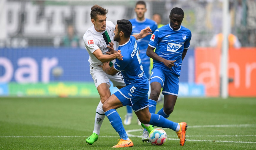 Gladbach-Profi Florian Neuhaus (l.) hat beim Bundesliga-Auftaktsieg im Borussia-Park gegen die TSG Hoffenheim (6. August 2022) einiges in den Zweikämpfen einstecken müssen und ist vor dem Schalke-Duell angeschlagen. Neuhaus wird vom Gegenspieler zur Seite gedrückt.