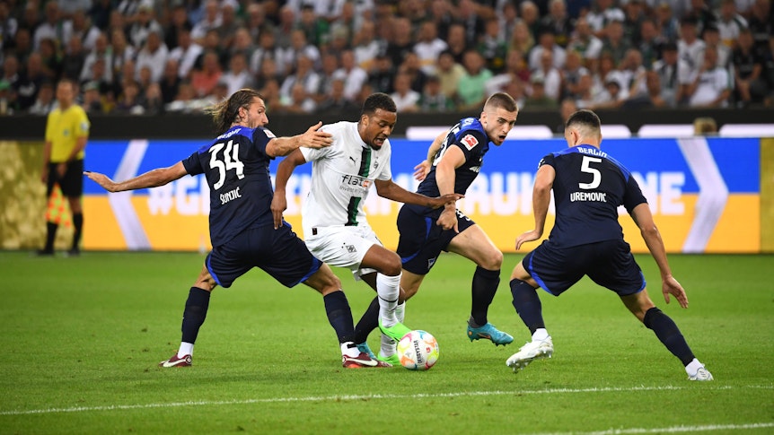 Gladbachs Alassane Plea (weiß, Mitte) im Zweikampf mit Berlins Ivan Sunjic (Nr. 34), Jonjoe Kenny (blau, Mitte) und Filip Uremovic (Nr. 5). Plea erzielte am 19. August 2022 die 1:0-Führung für Borussia Mönchengladbach gegen Hertha BSC per Elfmeter.
