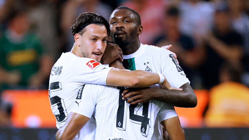 Gehen diese Gladbach-Profis bald getrennte Weg? Ramy Bensebaini (l.) und Marcus Thuram (r.) jubeln gemeinsam mit Alassane Plea (M.) am 19. August 2022 im Bundesliga-Duell gegen Hertha BSC. Die Spieler umarmen sich.