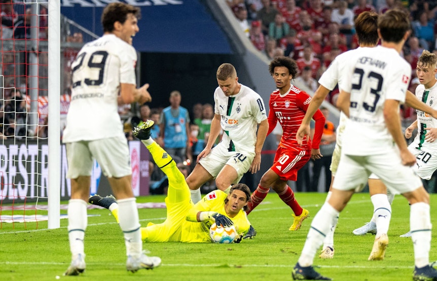 Yann Sommer, Torwart Borussia Mönchengladbach, liegt, umgeben von Spielern, auf dem Spielfeld und hält den Ball fest. Dieses Foto zeigt den Schweizer Nationalspieler am 27. August 2022 in der Allianz-Arena gegen Bayern München. Sommer trägt ein gelbes Trikot und schaut aufmerksam zur Seite.