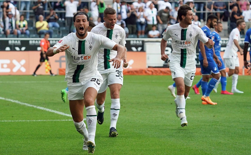 Gladbach-Profi Ramy Bensebaini (l.) bejubelt seinen Fallrückzieher-Treffer im Bundesliga-Duell gegen die TSG Hoffenheim am 6. August 2022 im Borussia-Park. Im Hintergrund sind seine Team-Kollegen Nico Elvedi und Joe Scally zu sehen.