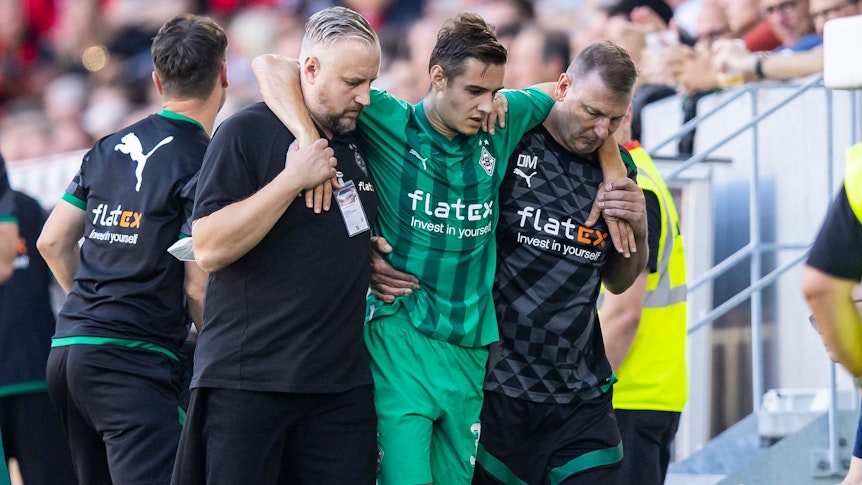 Gladbach-Profi Florian Neuhaus (M.) wird verletzt am Sonntag (11. September 2022) in Freiburg vom Platz getragen. Er wird von Betreuern gestützt.