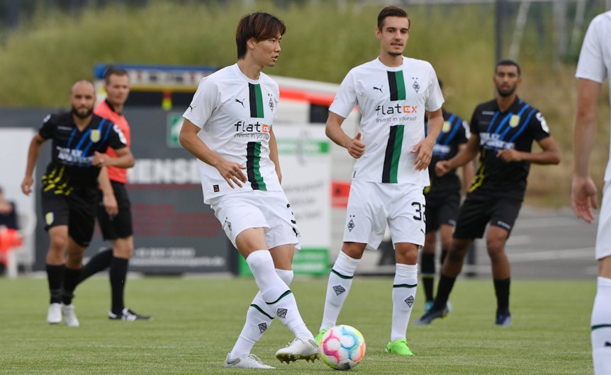 Die Gladbach-Profis Ko Itakura (l.) und Florian Neuhaus (r.) haben sich schwere Knieverletzungen zugezogen. Auf diesem Foto sind die beiden am 20. Juli 2022 bei einem Testspiel in Velbert zu sehen. Itakura hat den Ball am Fuß, Neuhaus schaut zu ihm.