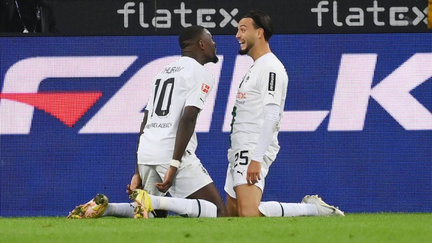 Gladbach-Profi Ramy Bensebaini (l.) jubelt gemeinsam mit Marcus Thuram über seinen Bundesliga-Treffer beim 3:0-Sieg gegen RB Leipzig am 17. September 2022 im Borussia-Park. Beide Spieler knien auf dem Rasen.