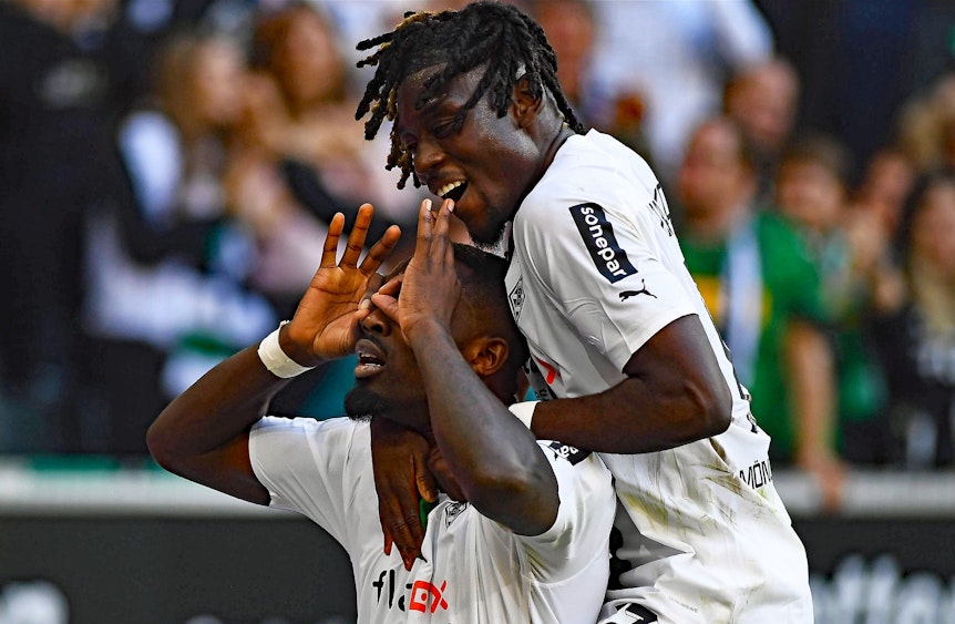 Stürmer Marcus Thuram (l.) von Borussia Mönchengladbach hat beim Derbysieg gegen den 1. FC Köln am Sonntag (9. Oktober 2022) zum 5:2-Endstand getroffen. Das Foto zeigt ihn beim Torjubel, bei dem er den Brillenjubel von Ex-Köln-Profi Anthony Modest imitiert. Teamkollege Manu Koné (r.) jubelt mit. Thuram macht eine Geste mit seinen Händen.
